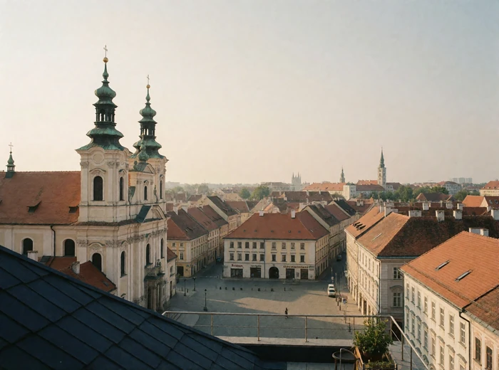 Elevated view over an Eastern European old town with terracotta rooftops, baroque spires and a cobbled square in warm daylight